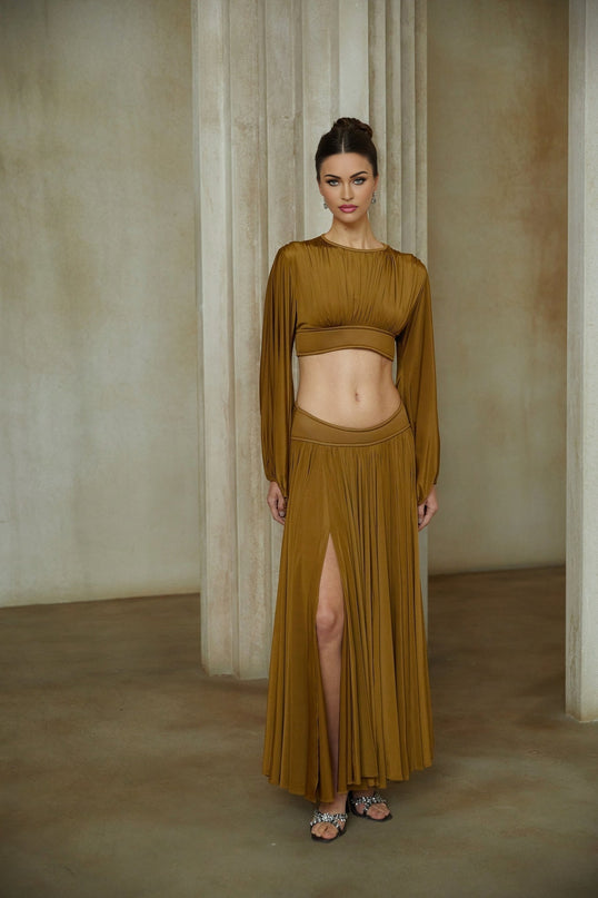 A woman wearing a vibrant green two piece outfit consisting of a fully pleated blouse and matching pleated skirt The ensemble has a feminine and elegant appearance with a flowing silhouette