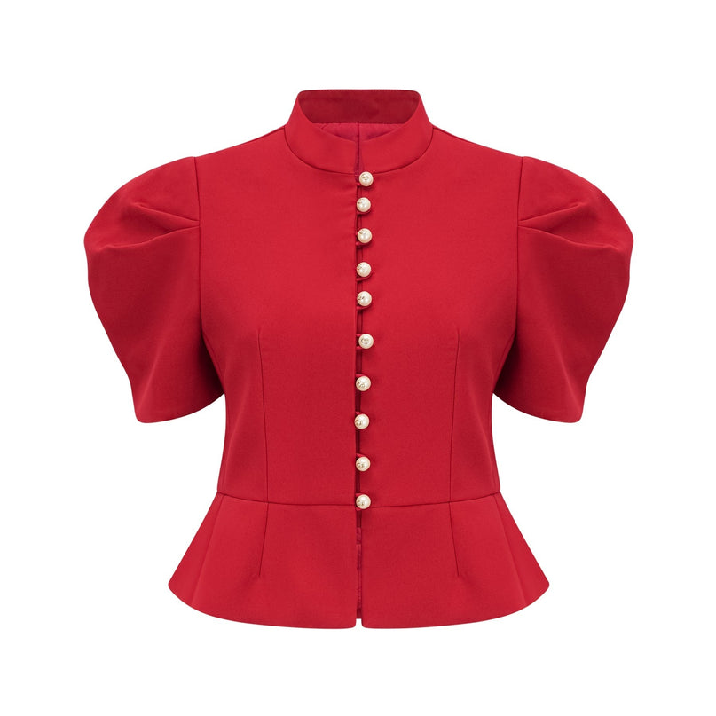 A woman wearing a vibrant red matching set consisting of a pleated blouse with a collar and a pleated skirt The blouse has long sleeves and the skirt falls to about knee length The outfit is styled as a coordinated ensemble named Colette
