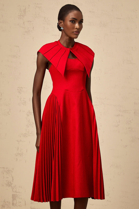 A woman wearing a vibrant red midi dress with a capelike design and pleated skirt standing in a neutral background
