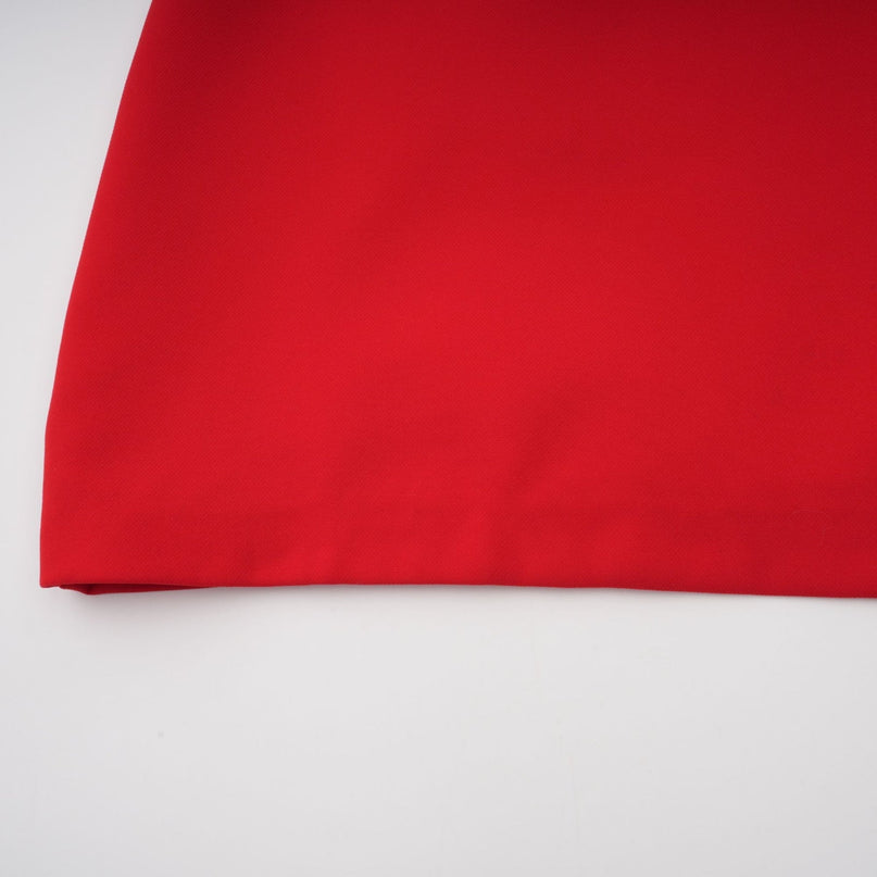 A woman wearing a vibrant red mini dress with cap sleeves standing against a plain background