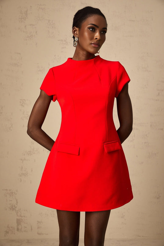 A woman wearing a vibrant red mini dress with cap sleeves standing against a plain background