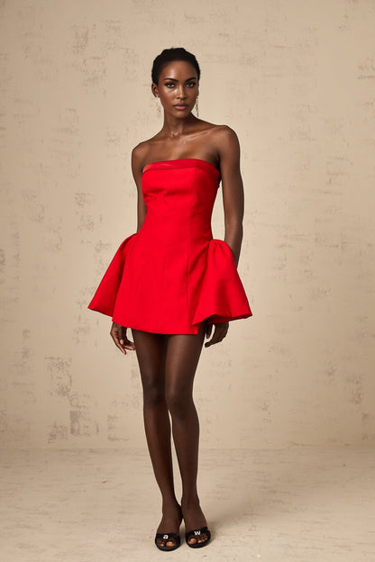 A woman wearing a vibrant red off shoulder mini dress with a flared skirt posing against a plain background