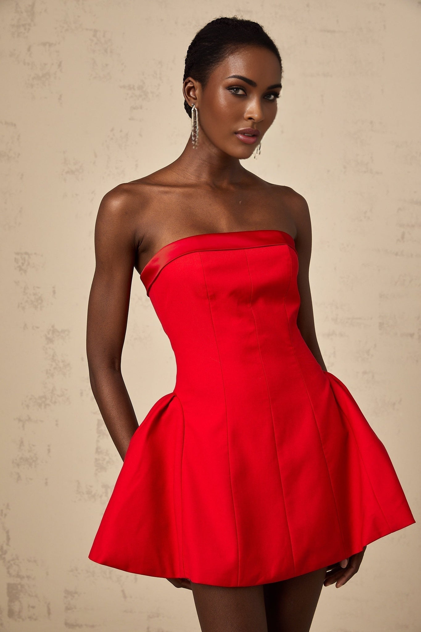 A woman wearing a vibrant red offshoulder mini dress with a flared skirt standing against a plain background