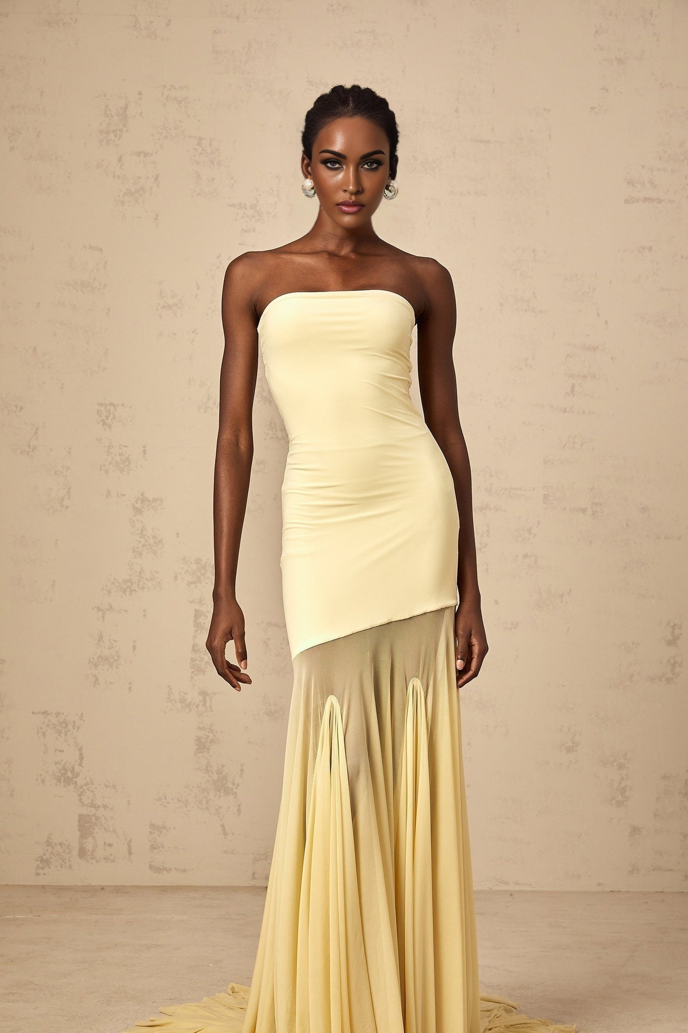 A woman wearing a vibrant yellow offshoulder maxi dress with sheer tulle detailing standing against a plain background