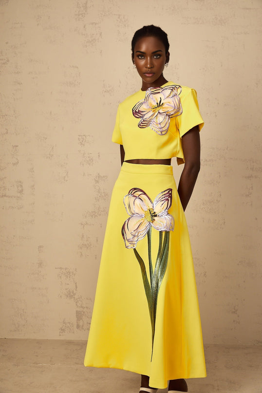 A woman wearing a vibrant yellow two piece outfit featuring sequin floral embroidery on both the top and bottom matching set