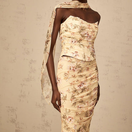 A woman wearing a vibrant yellow two piece outfit with a floral print design consisting of a fitted top and matching skirt