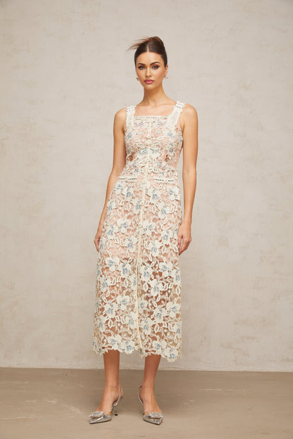 A woman wearing a white Aline midi dress with floral lace detailing standing in a neutral background