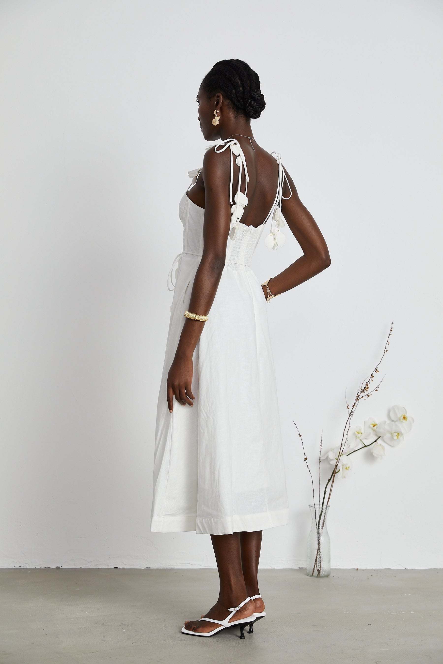 A woman wearing a white corset midi dress with a fitted bodice and flared skirt standing against a plain background