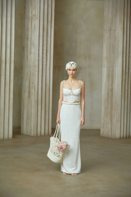 A woman wearing a white crochet knit top with short sleeves and a matching white crochet knit skirt standing against a plain background