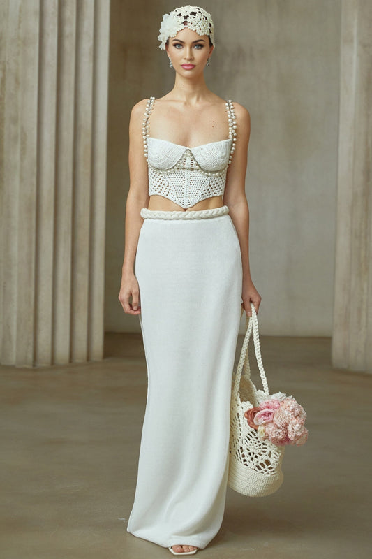 A woman wearing a white crochet knit two piece outfit consisting of a cropped top with short sleeves and a high waisted mini skirt The set features an intricate floral pattern throughout
