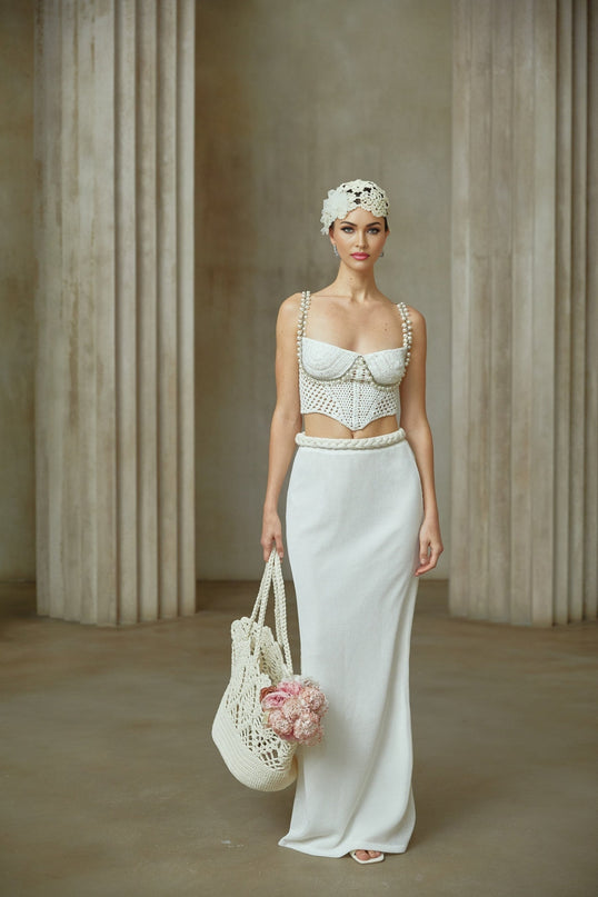 A woman wearing a white crochet knit two piece outfit consisting of a sleeveless crop top and matching high waisted mini skirt with a delicate floral pattern