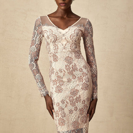 A woman wearing a white fitted midi dress with intricate guipure lace pattern standing against a plain background