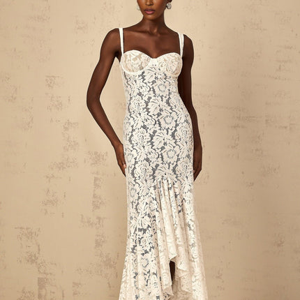 A woman wearing a white floral lace bustier maxi dress with a fitted bodice and flowing skirt standing against a plain background