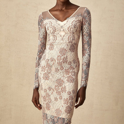 A woman wearing a white formfitting midi dress with intricate guipure lace patterns standing against a plain background