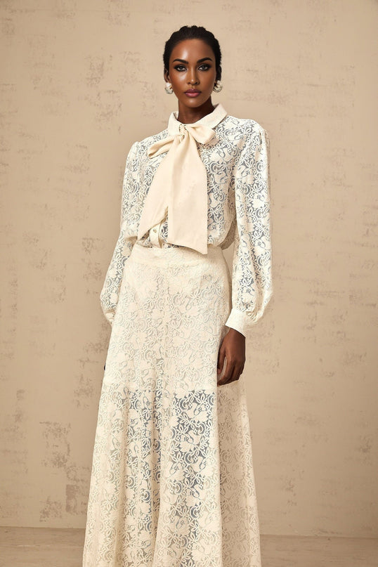 A woman wearing a white guipure lace matching set consisting of a shirt and trousers standing in a neutral pose