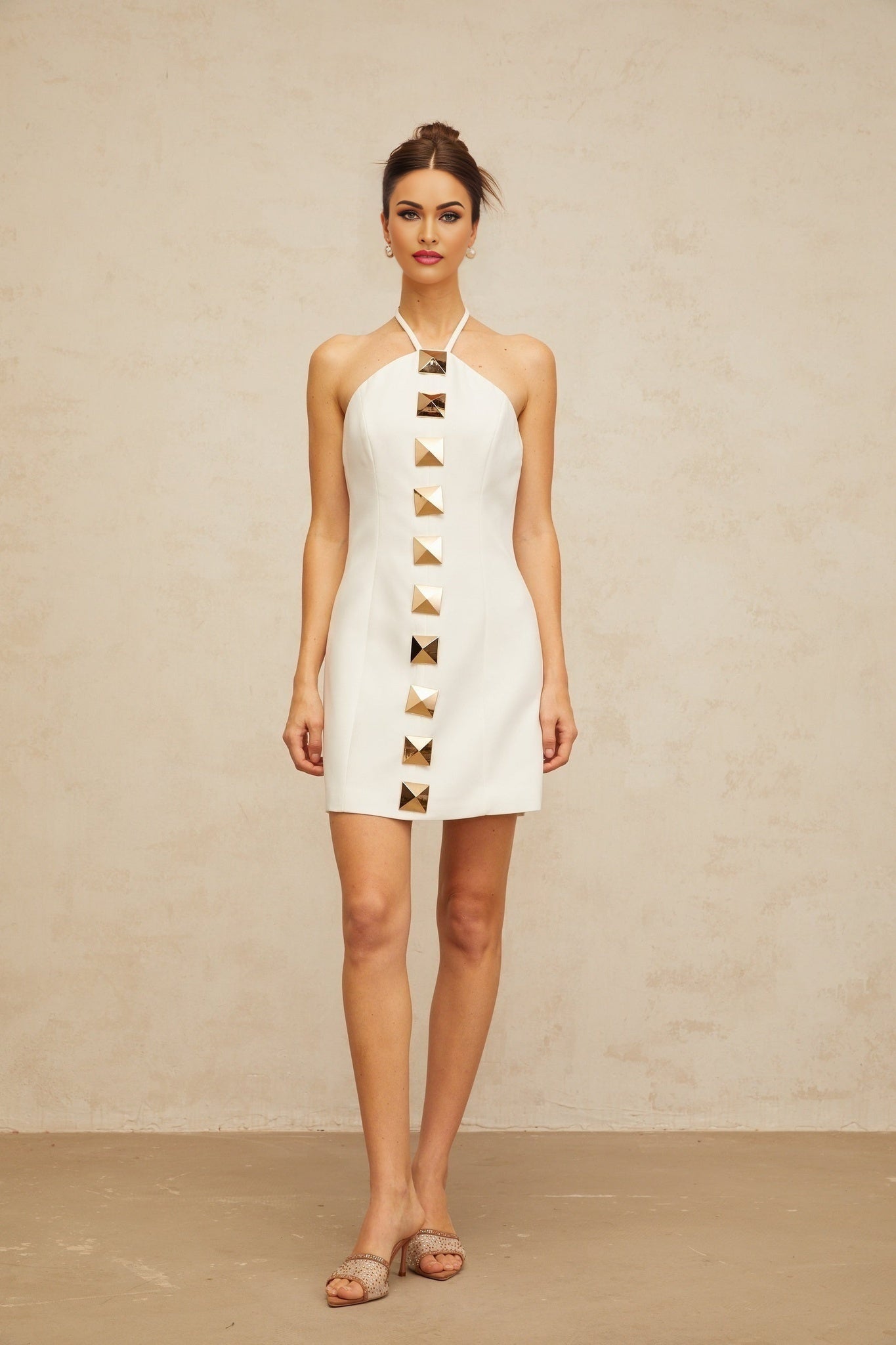 A woman wearing a white halterneck mini dress with an Aline silhouette standing against a plain background