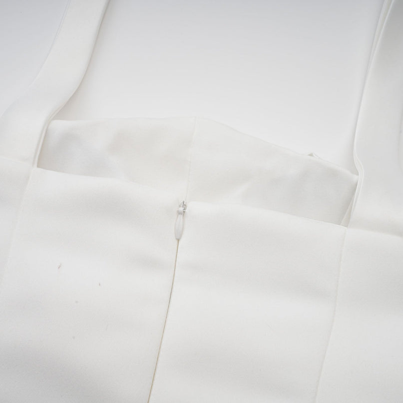 A woman wearing a white halterneck mini dress with ruffled details standing against a plain background