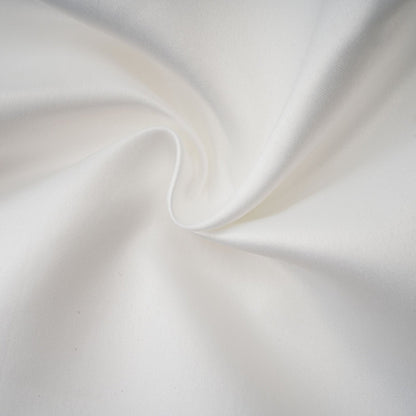 A woman wearing a white halterneck mini dress with ruffles standing against a plain background