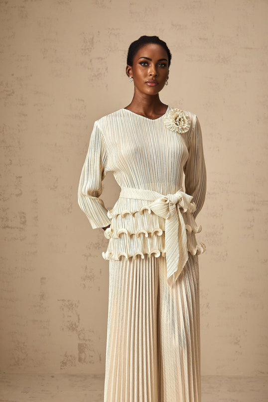 A woman wearing a white jumpsuit with floral appliques ruffles and pleated details