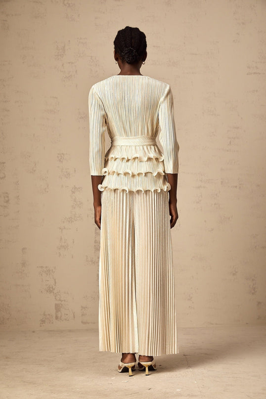 A woman wearing a white jumpsuit with floral appliques ruffles and pleated details