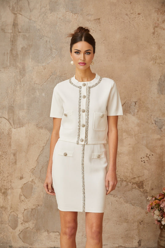 A woman wearing a white knit matching set consisting of a sleeveless top and skirt both embellished with crystal details