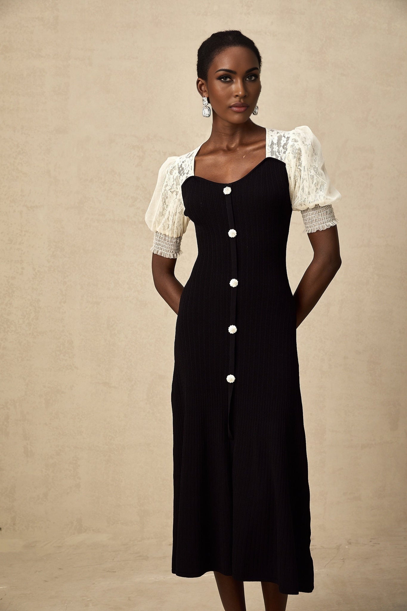 A woman wearing a white knit midi dress with delicate lace trim along the neckline and hem standing in a neutral background