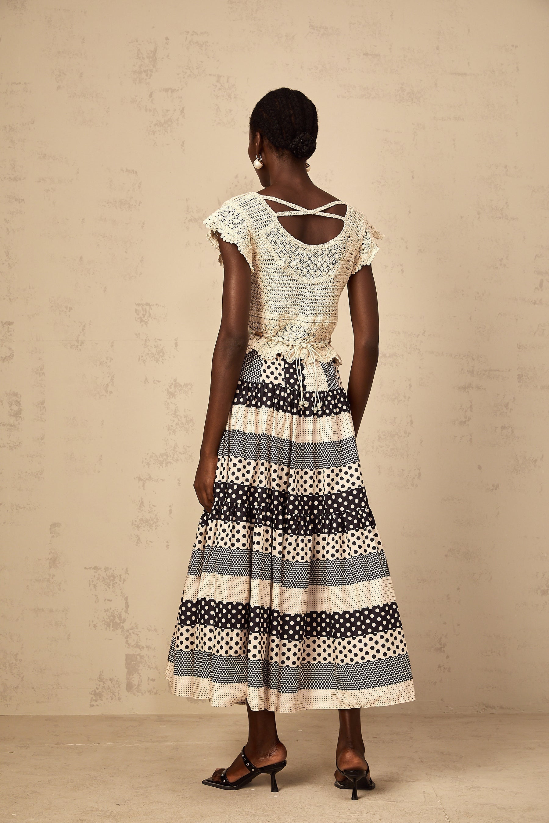 A woman wearing a white knit top with delicate 3D floral beaded details on the bodice showcasing intricate crochet work and a feminine design