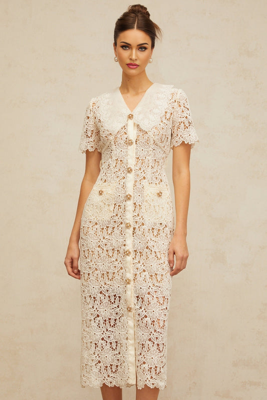 A woman wearing a white lace midi dress with a fitted bodice and flared skirt standing against a plain background