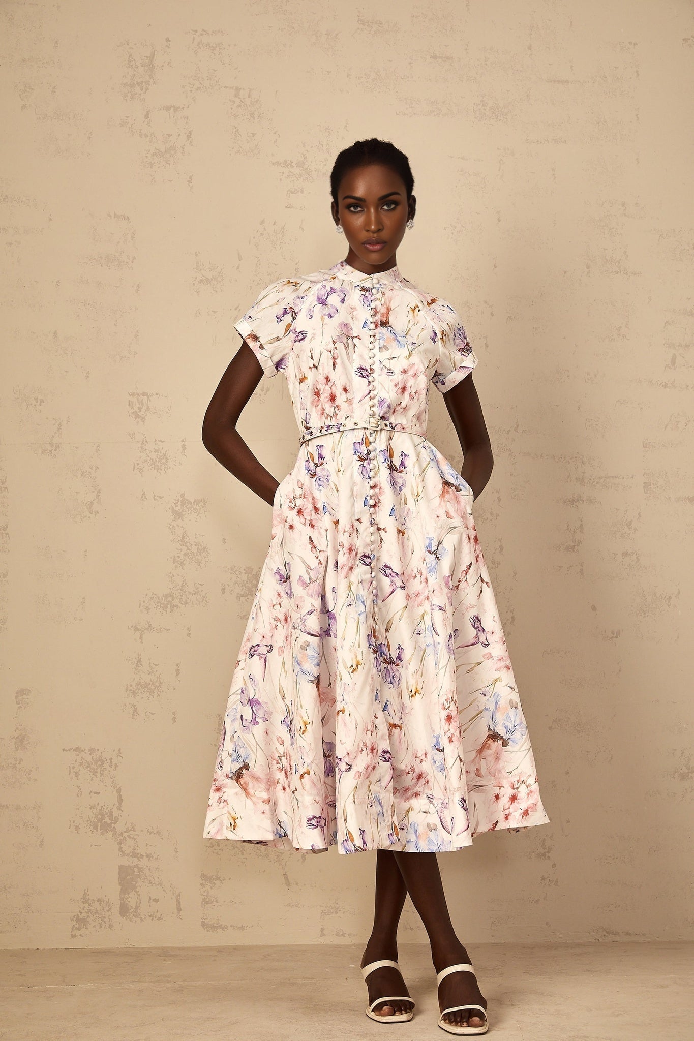A woman wearing a white midi dress with a mock neck and floral print standing in a relaxed pose