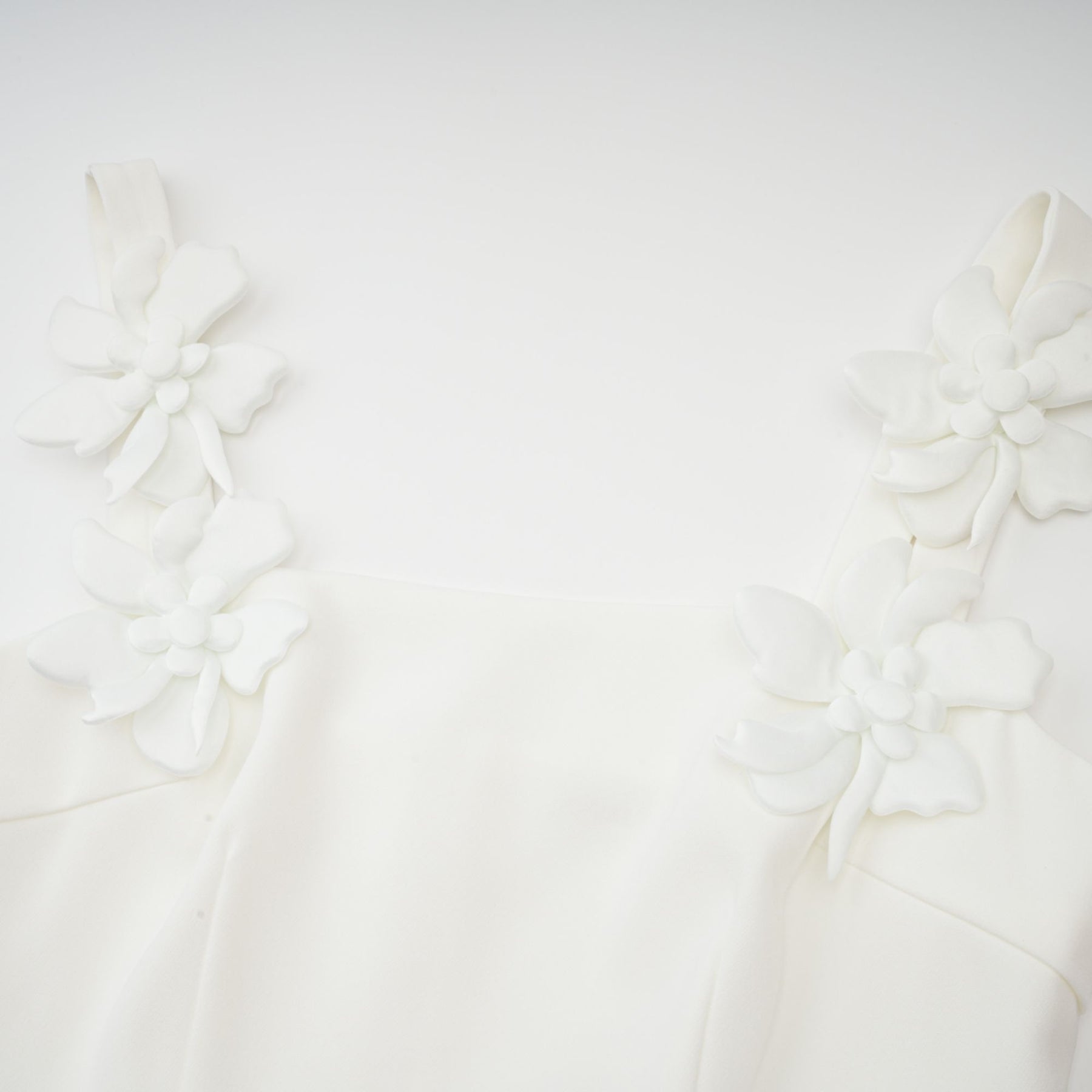 A woman wearing a white midi dress with a square neckline adorned with faux flowers standing against a plain background