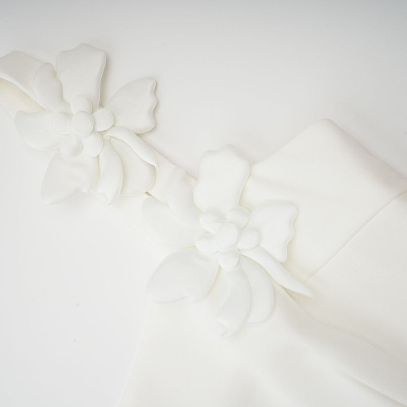 A woman wearing a white midi dress with a square neckline and faux flower details standing in a neutral background