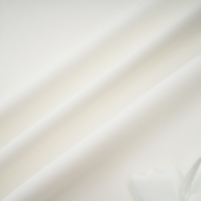 A woman wearing a white midi dress with a square neckline and faux flower details standing in a neutral setting