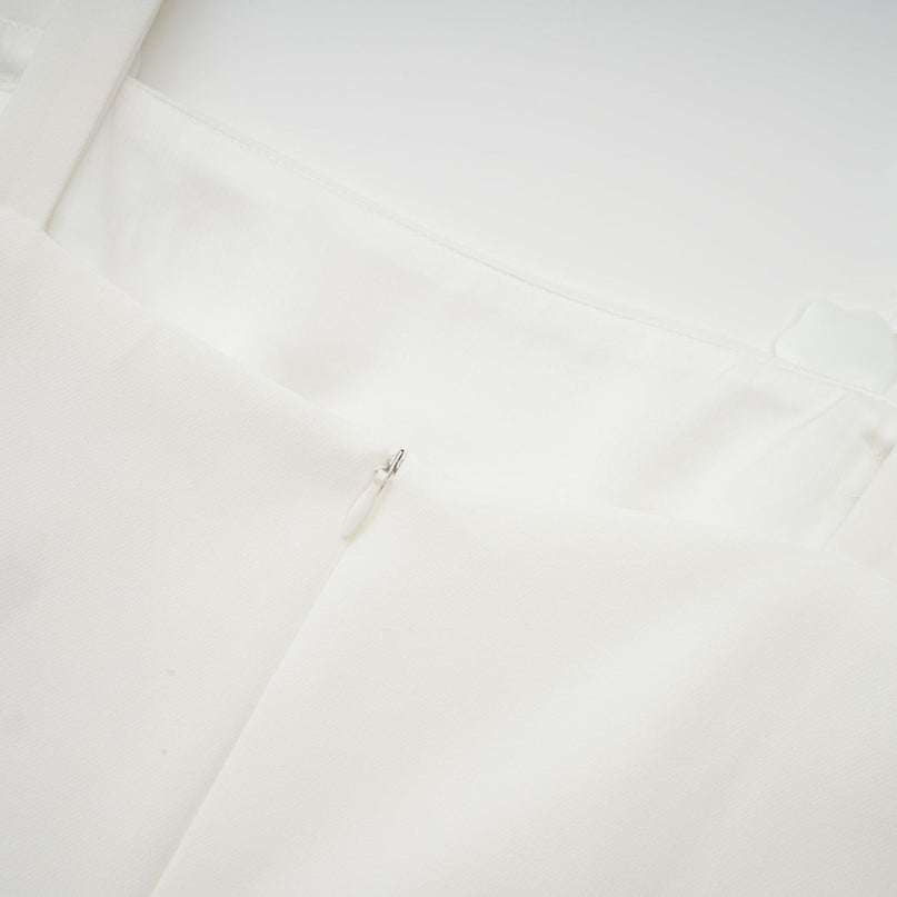 A woman wearing a white midi dress with a square neckline and faux flower details standing in a neutral setting