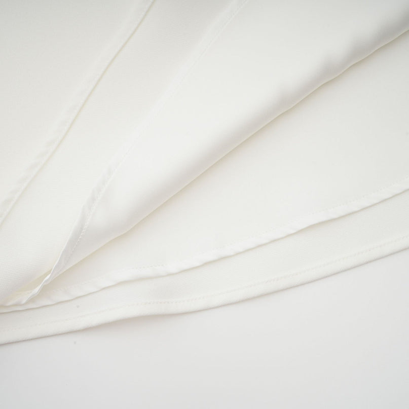 A woman wearing a white midi dress with a square neckline and faux flower embellishments standing in a neutral background
