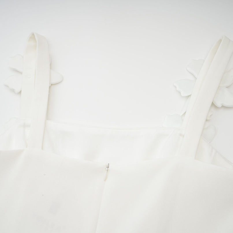 A woman wearing a white midi dress with a square neckline and faux flower embellishments standing in a relaxed pose