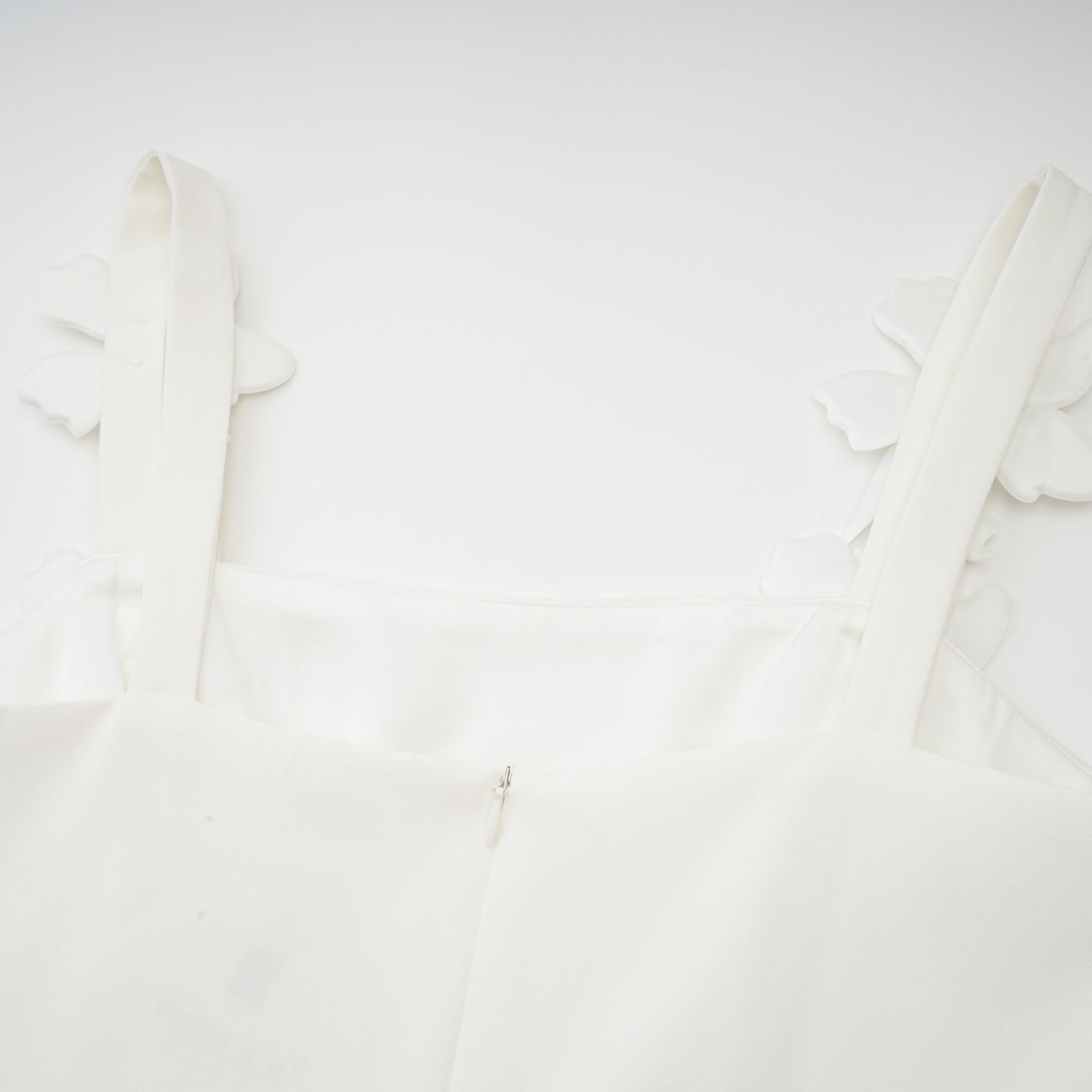 A woman wearing a white midi dress with a square neckline and faux flower embellishments standing in a relaxed pose