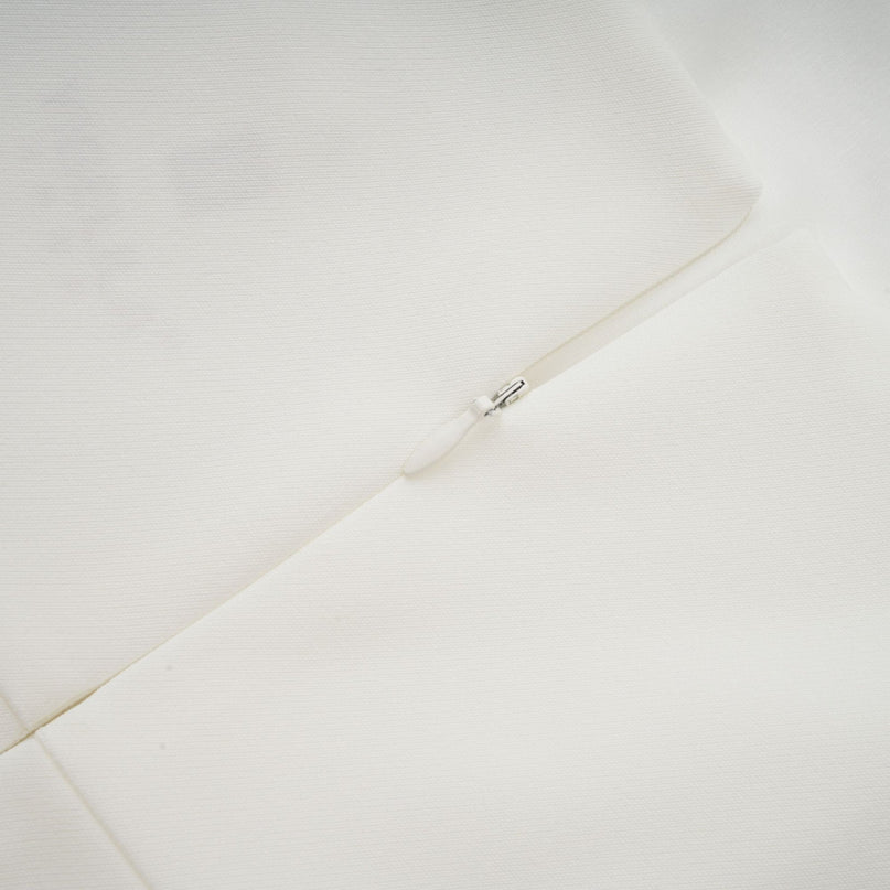 A woman wearing a white midi dress with a square neckline featuring faux flower embellishments standing in a neutral pose