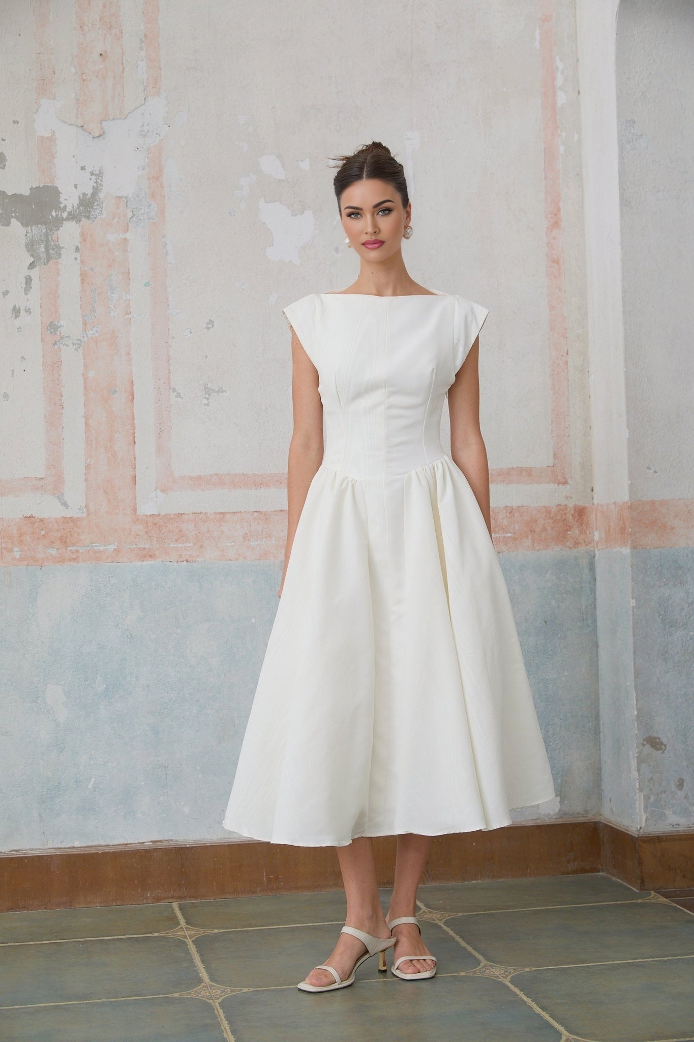 A woman wearing a white midi dress with cap sleeves and an open back design standing in a relaxed pose
