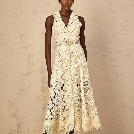 A woman wearing a white midi dress with colorful floral embroidery and cutout details standing against a plain background