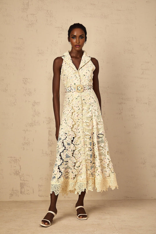 A woman wearing a white midi dress with colorful floral embroidery and cutout details standing against a plain background