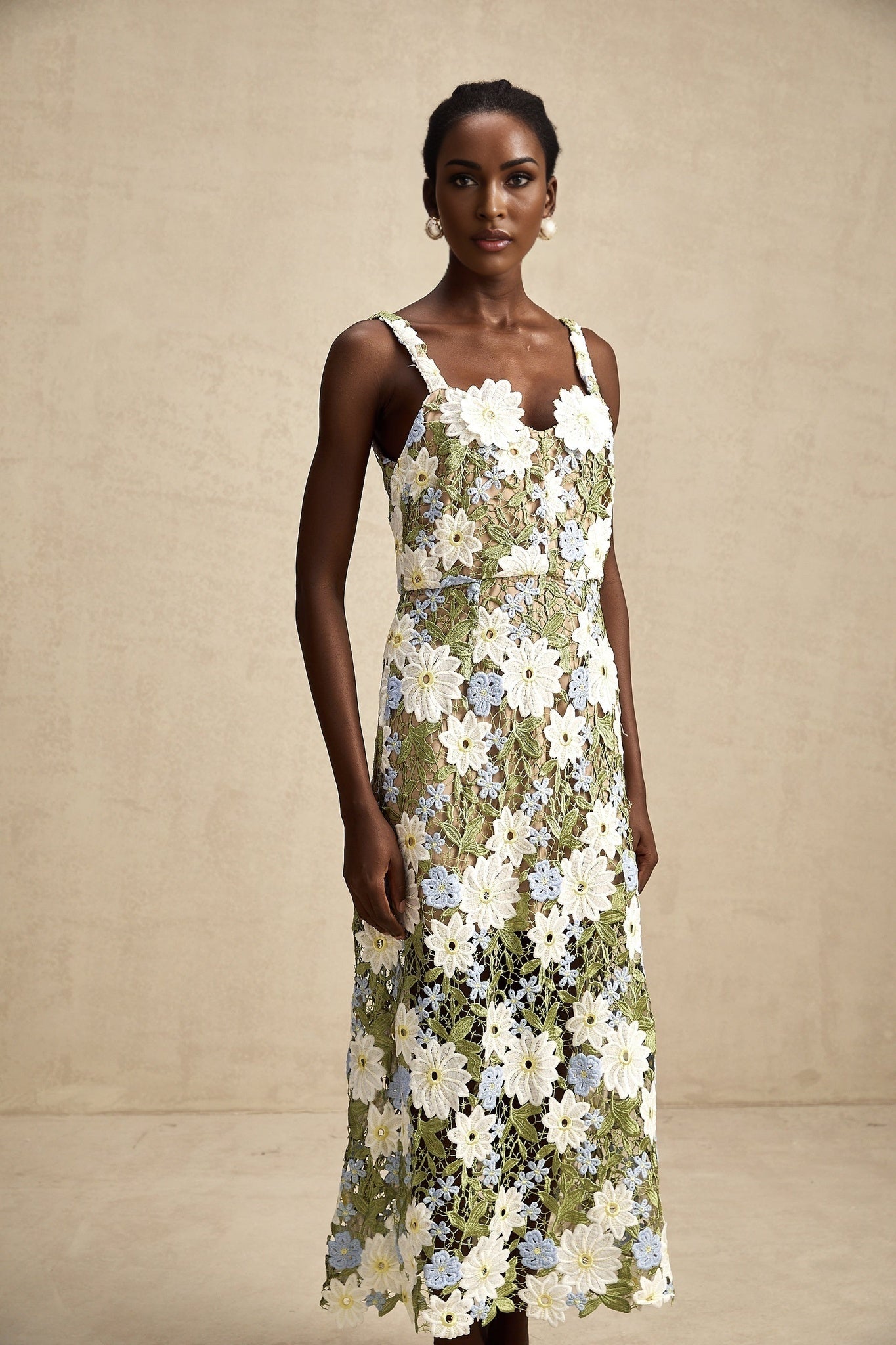 A woman wearing a white midi dress with colorful floral embroidery and delicate cutout patterns throughout the fabric