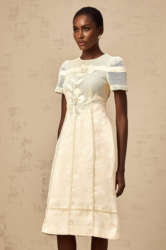 A woman wearing a white midi dress with colorful floral embroidery and openwork details standing in a neutral background