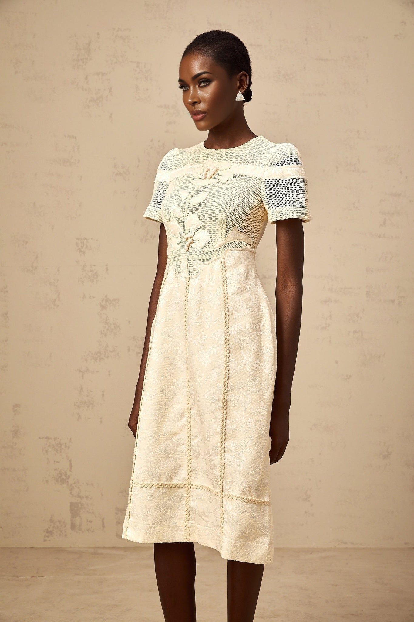 A woman wearing a white midi dress with colorful floral embroidery and openwork details standing in a relaxed pose