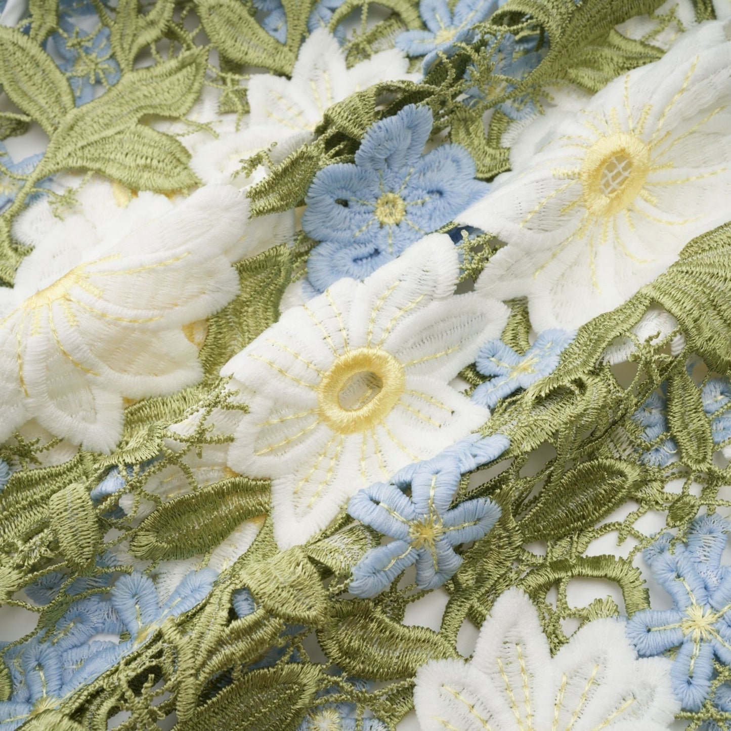 A woman wearing a white midi dress with floral embroidery and cutout details standing against a plain background
