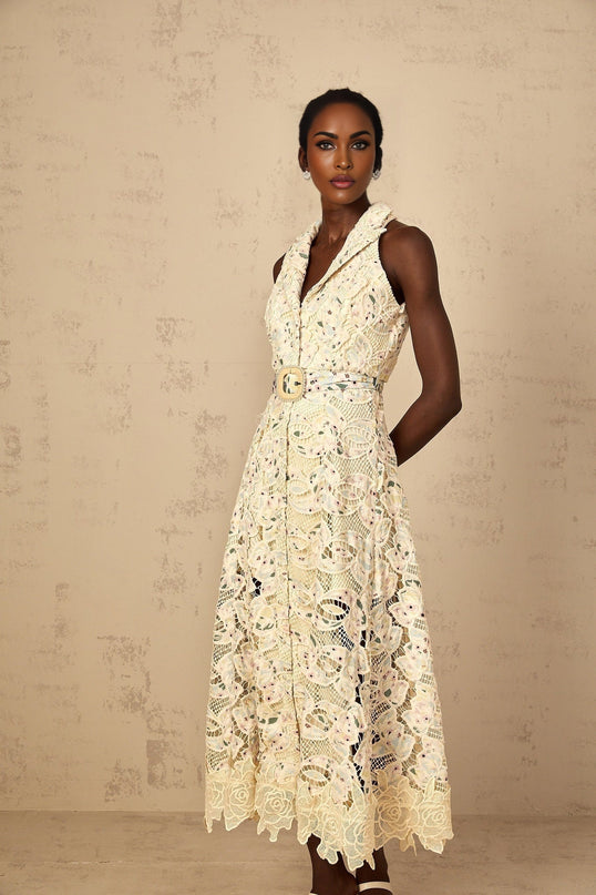 A woman wearing a white midi dress with floral embroidery and cutout details standing in a relaxed pose