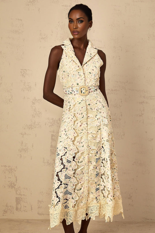 A woman wearing a white midi dress with floral embroidery and cutout details standing in a relaxed pose