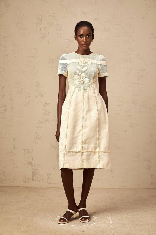A woman wearing a white midi dress with floral embroidery and openwork details standing in a relaxed pose