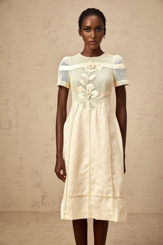 A woman wearing a white midi dress with floral embroidery and openwork details standing in a relaxed pose