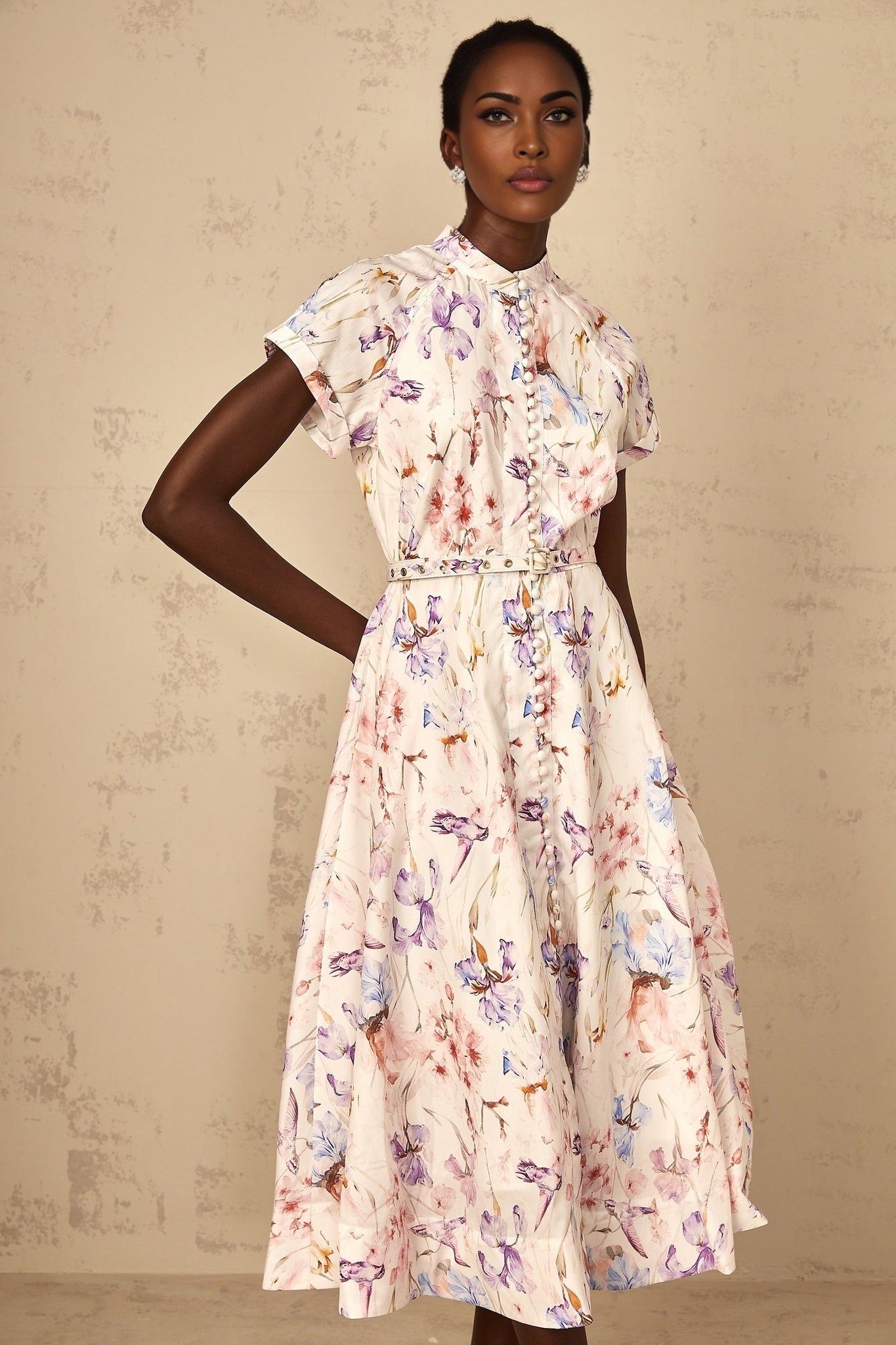 A woman wearing a white midi dress with floral print and mock neck design standing in a neutral background