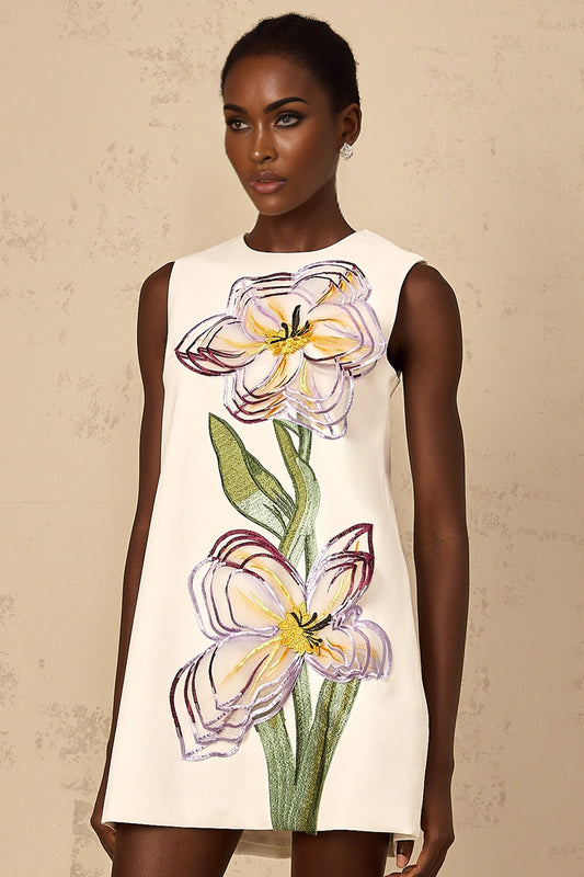 A woman wearing a white mini dress with sequin floral embroidery details standing in a relaxed pose against a plain background